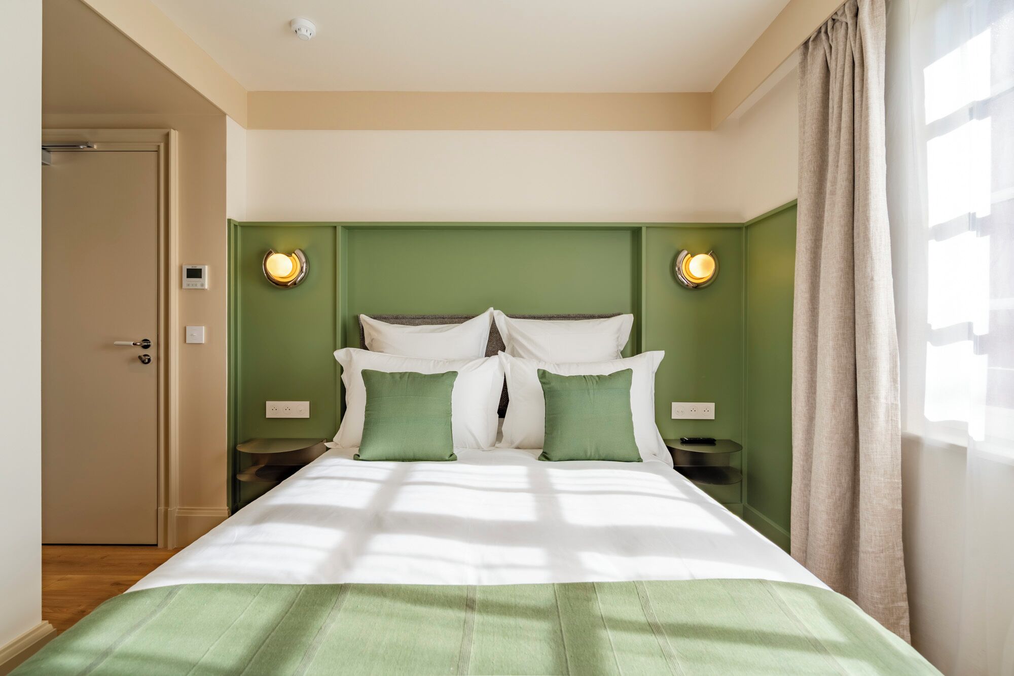 A hotel room with a bed, green walls, two bedside lamps, and a door.