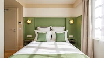 A hotel room with a bed, green walls, two bedside lamps, and a door.