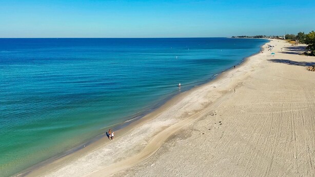 A beach with clear blue water, a sandy shore, and a few people walking along the beach. - Sunrays Anchor by Duncan Real Estate (Holmes Beach)