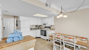 A compact kitchen with white cabinets, a stove, microwave, and a dining area with a wooden table and chairs. - Sunrays Anchor by Duncan Real Estate (Holmes Beach)