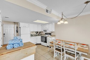 A compact kitchen with white cabinets, a stove, microwave, and a dining area with a wooden table and chairs. - Sunrays Anchor by Duncan Real Estate (Holmes Beach)
