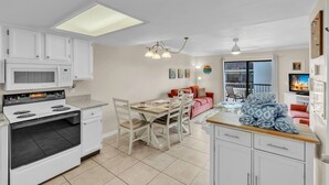 A compact kitchen with white cabinets, a microwave, a stove, and a dining area with a table and chairs. - Sunrays Anchor by Duncan Real Estate (Holmes Beach)