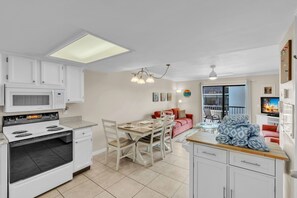 A compact kitchen with white cabinets, a microwave, a stove, and a dining area with a table and chairs. - Sunrays Anchor by Duncan Real Estate (Holmes Beach)