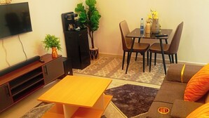 Una sala de estar con televisor, sofá, mesa de centro, mesa de comedor con sillas y aparador.
