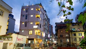 Un immeuble à plusieurs étages doté de balcons, une voiture garée et une rue bordée de boutiques.