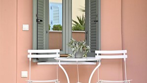 A white metal table with two chairs, a potted plant, and a hanging light fixture in front of a door with green shutters. - Ma Maison N°10 Elegant Plaka Villa under Acropolis (Athens)