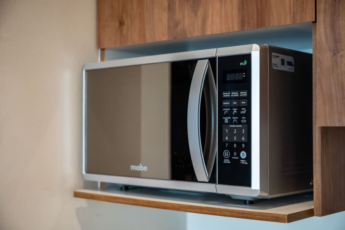Un four à micro-ondes moderne doté d’un écran numérique et d’un panneau de commande, placé sur une étagère en bois dans une cuisine.