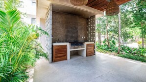 Un espace extérieur aménagé avec une structure en béton, des bancs en bois et des lampes en osier suspendues.