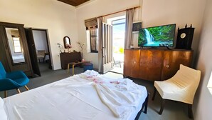 Un dormitori amb llit, televisió, rellotge, tocador i cadira.