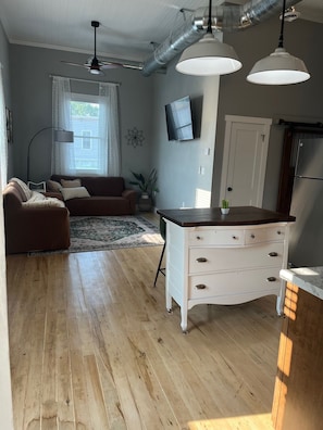 A living room with a sofa, a coffee table, a TV, and a kitchen area with a fridge.