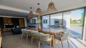 Un comedor moderno con una mesa de madera y sillas tejidas, ventanas amplias y vistas al exterior.
