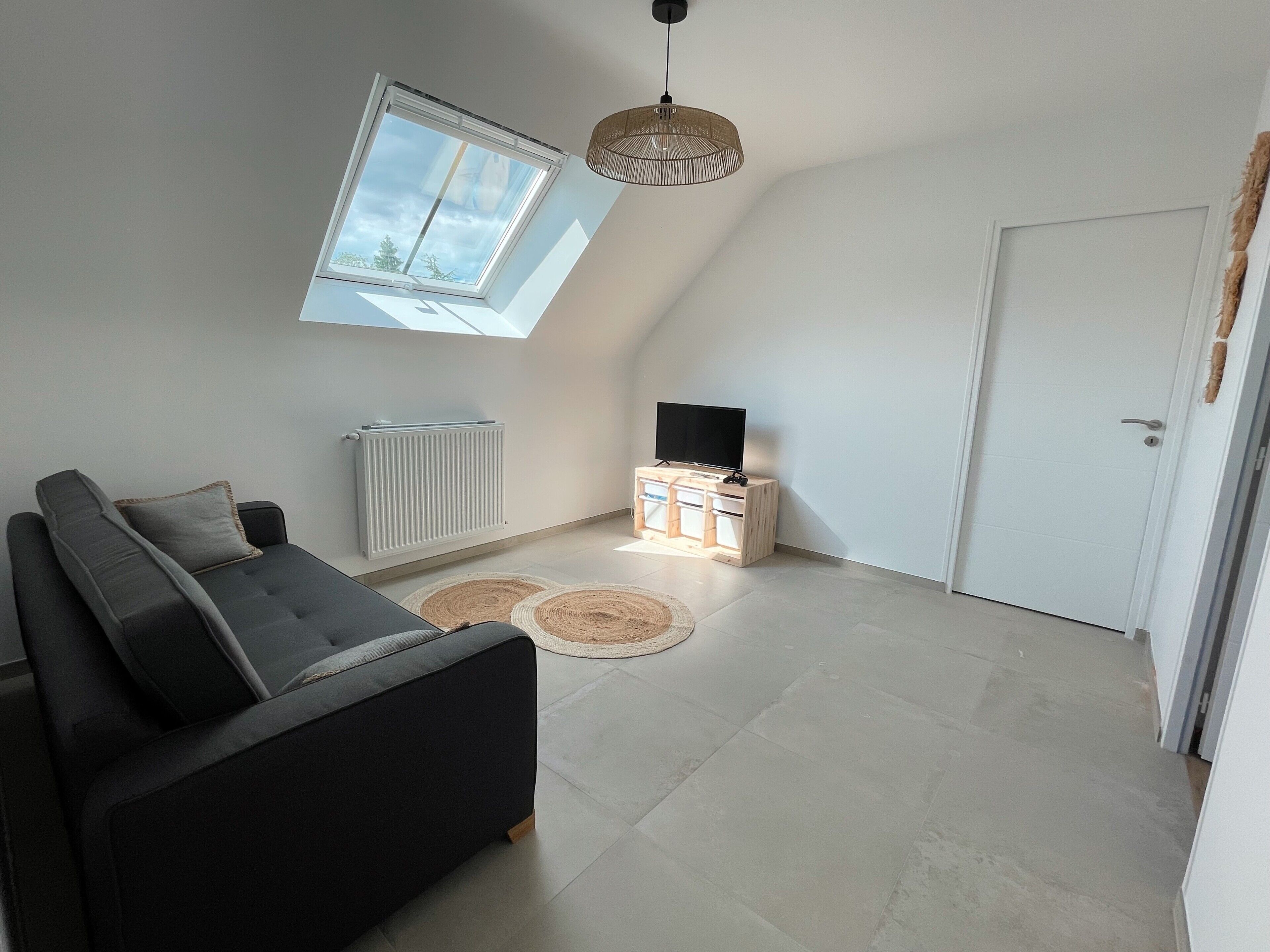 A modern living room with a sofa, a television on a wooden stand, a radiator, and a skylight.