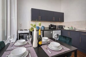A modern kitchen with dark cabinets, a dining table set with white plates, glasses, and a bottle of wine. - Winter Sale! Newcastle's Most Central Apartment (Newcastle upon Tyne)