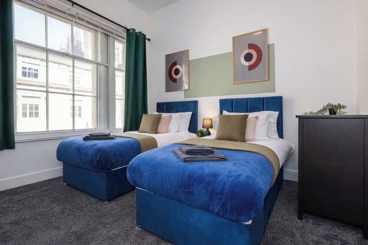Habitación de hotel con dos camas, una ventana con cortinas y una obra de arte en la pared.