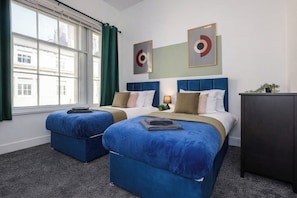 A hotel room with two beds, a window with curtains, and artwork on the wall. - Winter Sale! Newcastle's Most Central Apartment (Newcastle upon Tyne)