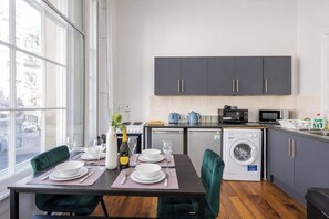 A modern kitchen with grey cabinets, a washing machine, and a dining area with a table set for two. - Winter Sale! Newcastle's Most Central Apartment (Newcastle upon Tyne)