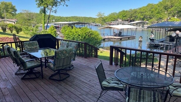 Um deck de madeira com móveis de exterior, piscina e barcos ao fundo.