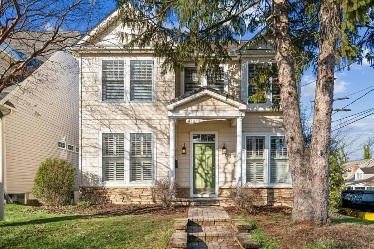 A two-story house with a front porch, a green door, and a stone foundation.
