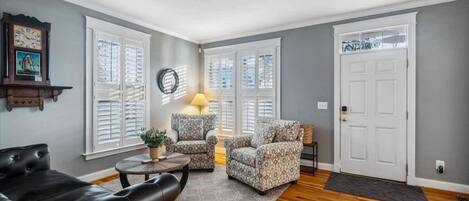A living room with a leather sofa, patterned armchairs, a round coffee table, and a lamp.