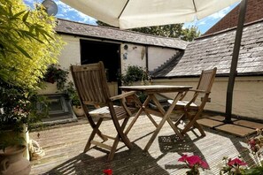 Eine Terrasse im Freien mit Tisch und Stühlen, einem überdachten Bereich und Topfpflanzen.