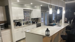 Une cuisine moderne avec des meubles blancs, un îlot central et des luminaires suspendus.