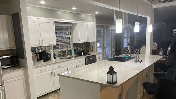 Une cuisine moderne avec des meubles blancs, un îlot central et des luminaires suspendus.