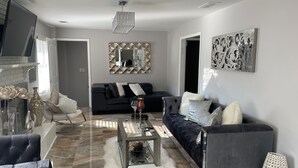 Un salon moderne avec un canapé noir, une table basse en verre et un tapis blanc à poils longs.