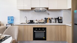 Une cuisine moderne avec des meubles blancs, un four encastré, une cuisinière et une machine à café.