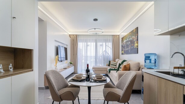 Una sala moderna con una mesa de comedor, dos sillas, un sofá, un televisor y una zona de cocina con dispensador de agua.