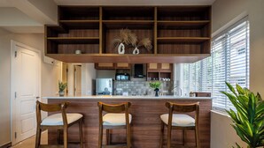 A kitchen with a wooden bar, three bar stools, a microwave, and a potted plant. - Staymaster Solintra 3BHK C301 (Verem)
