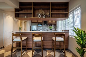 A kitchen with a wooden bar, three bar stools, a microwave, and a potted plant.