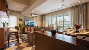 A modern kitchen with a dining area, large windows, and a flat-screen TV. - Staymaster Solintra 3BHK C301 (Verem)