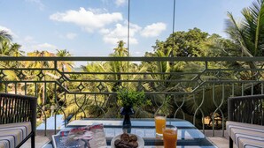 A balcony with a table, a magazine, cookies, and a glass of orange juice. - Staymaster Solintra 3BHK C301 (Verem)