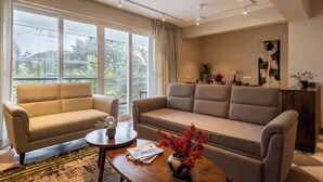 Ein modernes Wohnzimmer mit zwei Sofas, einem Couchtisch und einem großen Fenster mit Blick ins Grüne.