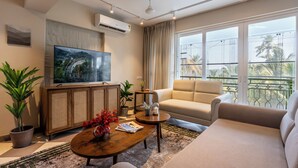 A modern living room with a flat-screen TV, a sofa, a coffee table, and potted plants. - Staymaster Solintra 3BHK C301 (Verem)