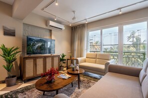 Ein modernes Wohnzimmer mit Flachbildfernseher, einer Couch, einem Couchtisch und Topfpflanzen.