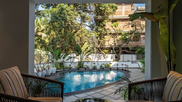 A pool area with a circular shape, surrounded by potted plants and two wicker chairs. - Staymaster Solintra 3BHK C301 (Verem)