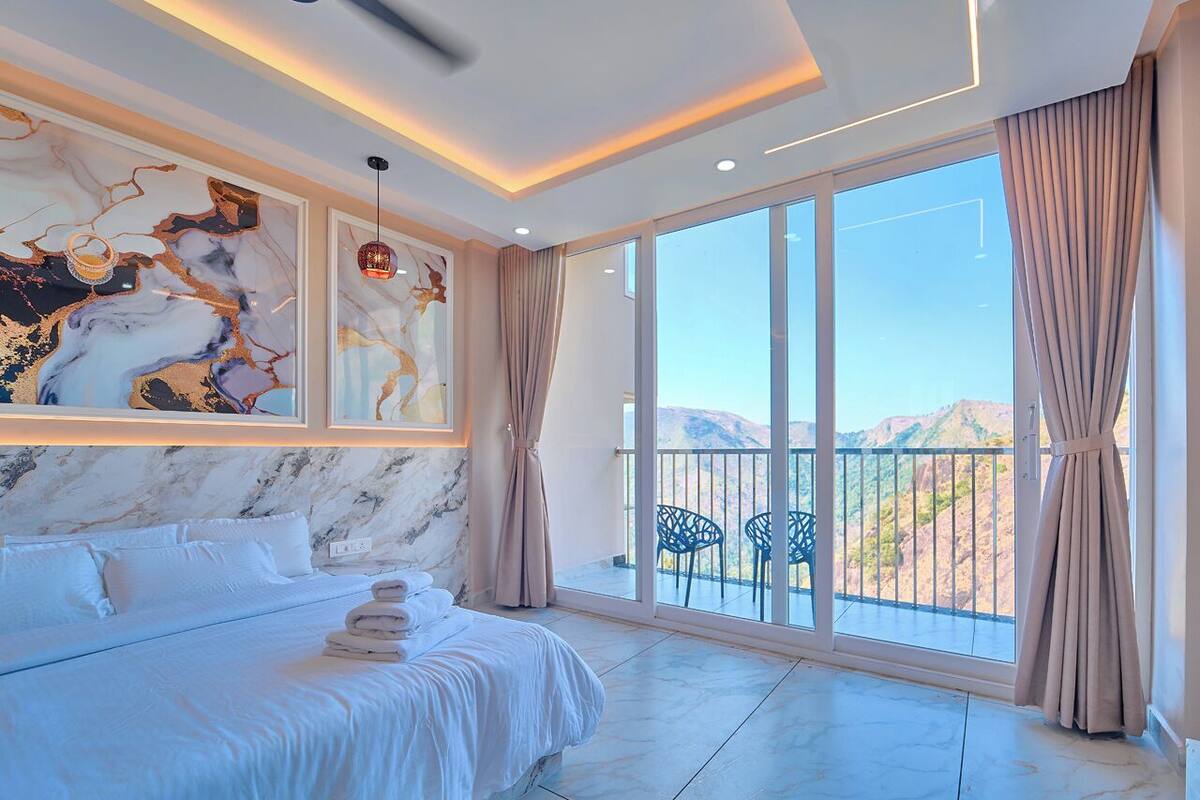Een slaapkamer met een groot bed, een marmeren wand, een balkon met stoelen en uitzicht op een berg.