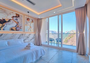 Ein Schlafzimmer mit einem großen Bett, einer Marmorwand, einem Balkon mit Stühlen und Blick auf die Berge.
