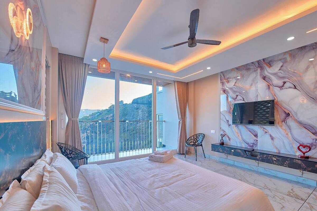 Een moderne slaapkamer met een groot bed, een plafondventilator, een televisie en een balkon met uitzicht.