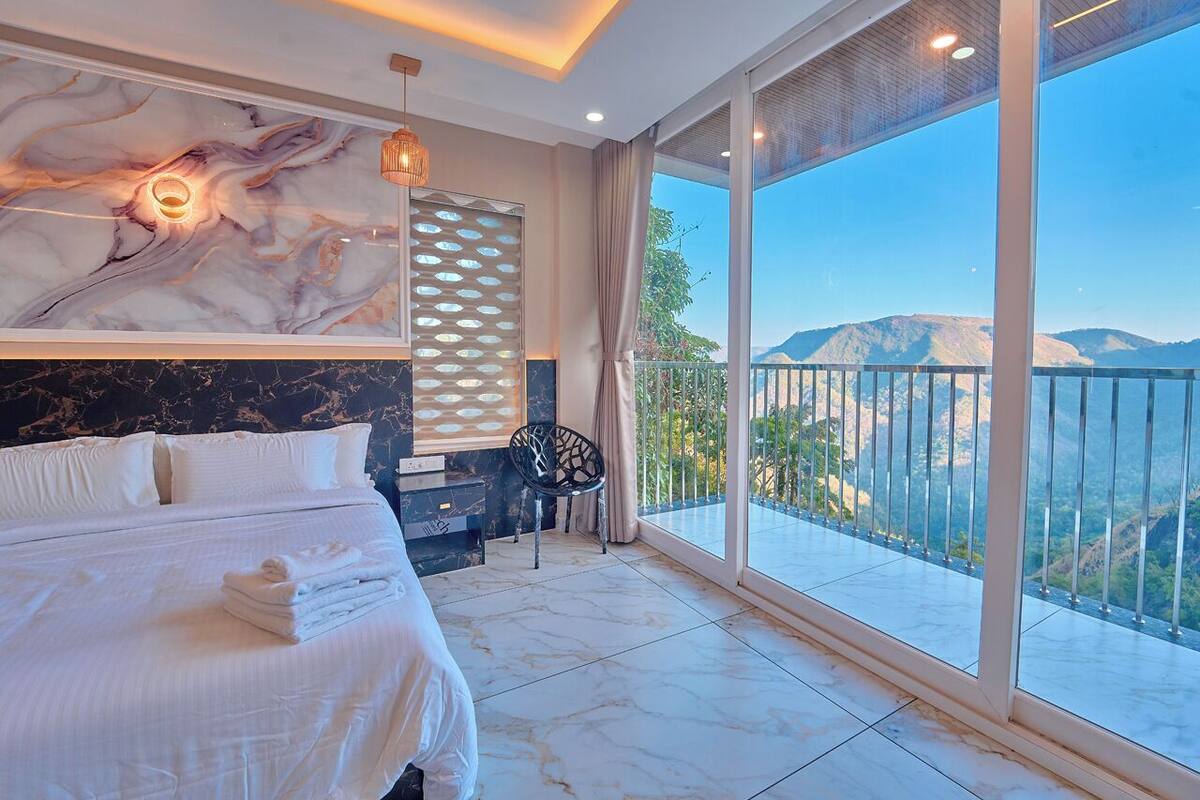 Een slaapkamer met een groot bed, een stoel, uitzicht op bergen en een balkon.