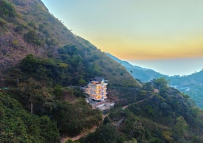 A multi-story building with a flat roof, surrounded by dense forest and hills. - Hill Breeze Resort by VOYE HOMES (Peermade)