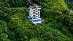 Ein mehrstöckiges Gebäude mit Schwimmbad, umgeben von üppiger Vegetation und einer Serpentinenstraße.