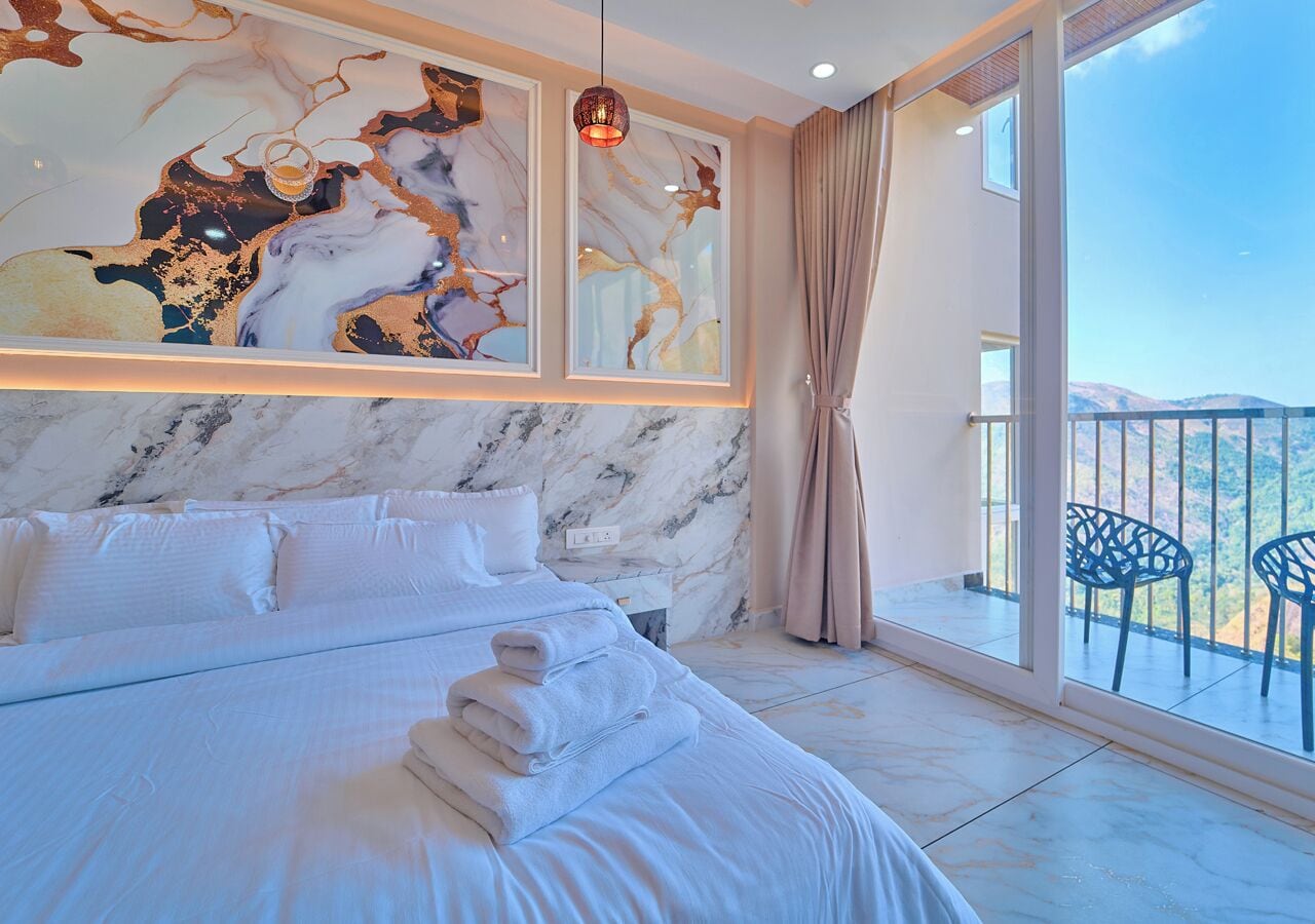 A modern hotel room with a large bed, a marble wall, a balcony with chairs, and artwork above the bed.