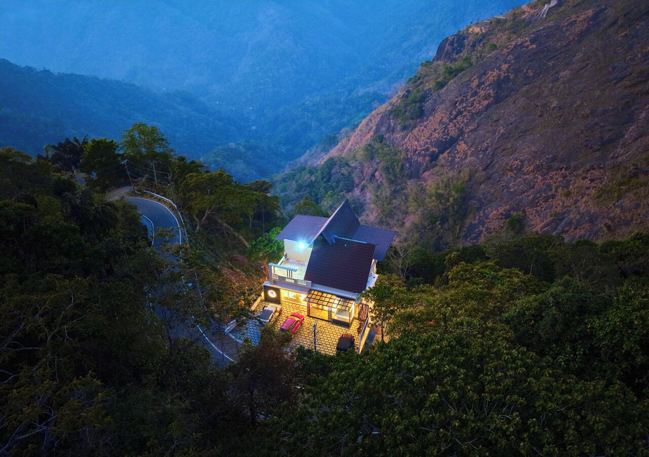 Una casa con techo inclinado, rodeada de un bosque frondoso y un camino sinuoso cerca.