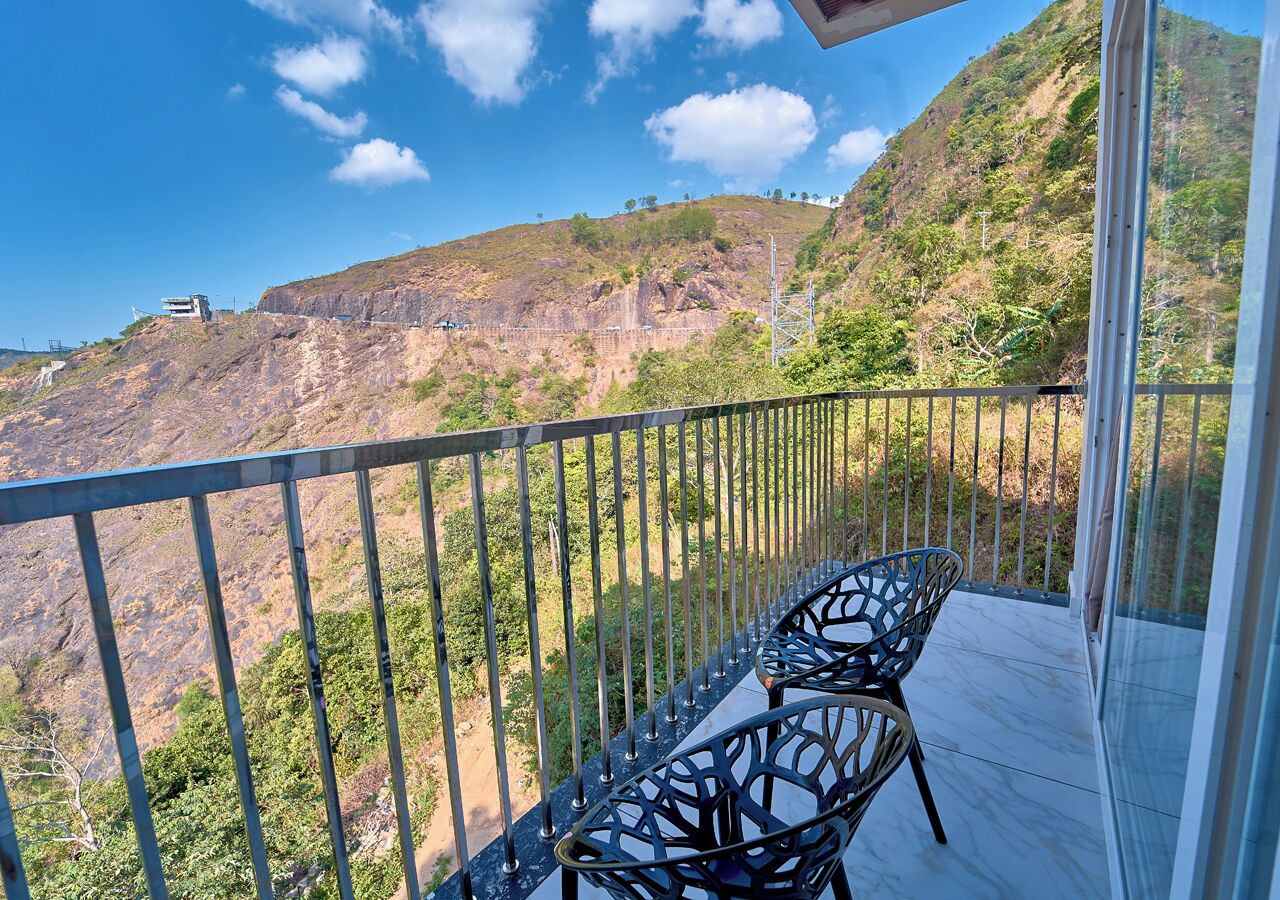 Een balkon met een metalen hekwerk, twee stoelen en uitzicht op een bergachtig landschap.