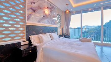A large bed with a white bedspread, a marble headboard, and a view of the outdoors.