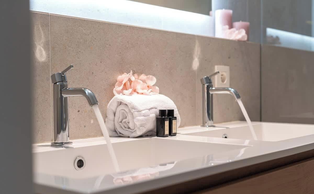 Une salle de bain avec un miroir, deux robinets, une serviette et un flacon de lotion.