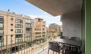 Un balcón con mesa y sillas, con vistas a un paisaje urbano con varios edificios.