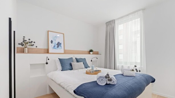 A modern bedroom with a bed, pillows, a bedside table, a framed picture, and a window with curtains. - Duin & Kust Residence - 50 metres from the beach, promenade and dunes (Oostduinkerke)